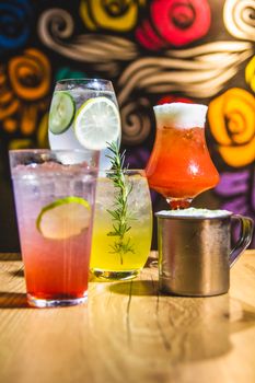 Colorful variety of cocktails in vibrant glassware on a wooden table in a modern bar setting.