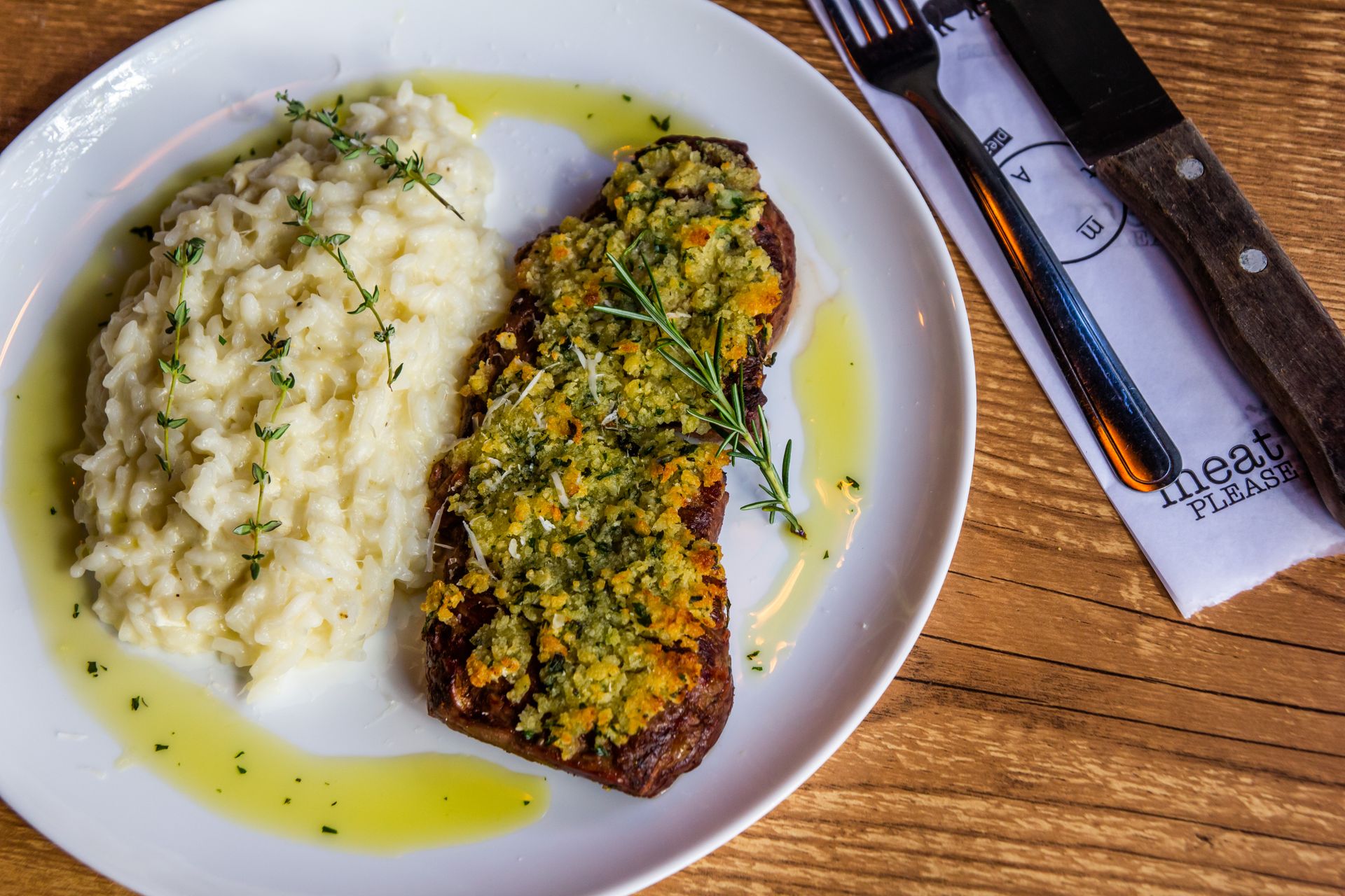 Delicious herb-crusted steak paired with creamy risotto on a white plate, artfully presented.