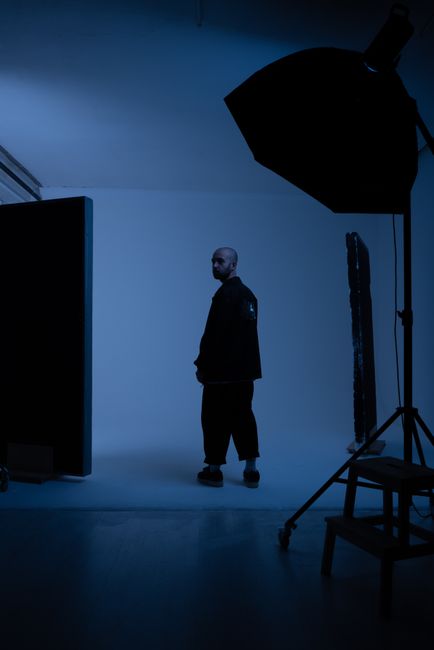 A male model poses dramatically in a dimly lit studio with blue lighting.