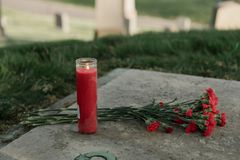 A red candle and carnations resting on a grave, symbolizing remembrance and tribute.