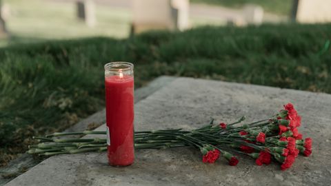A red candle and carnations resting on a grave, symbolizing remembrance and tribute.