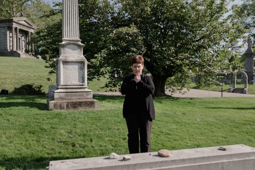 Woman stands thoughtfully in a serene cemetery, surrounded by monuments and lush greenery.