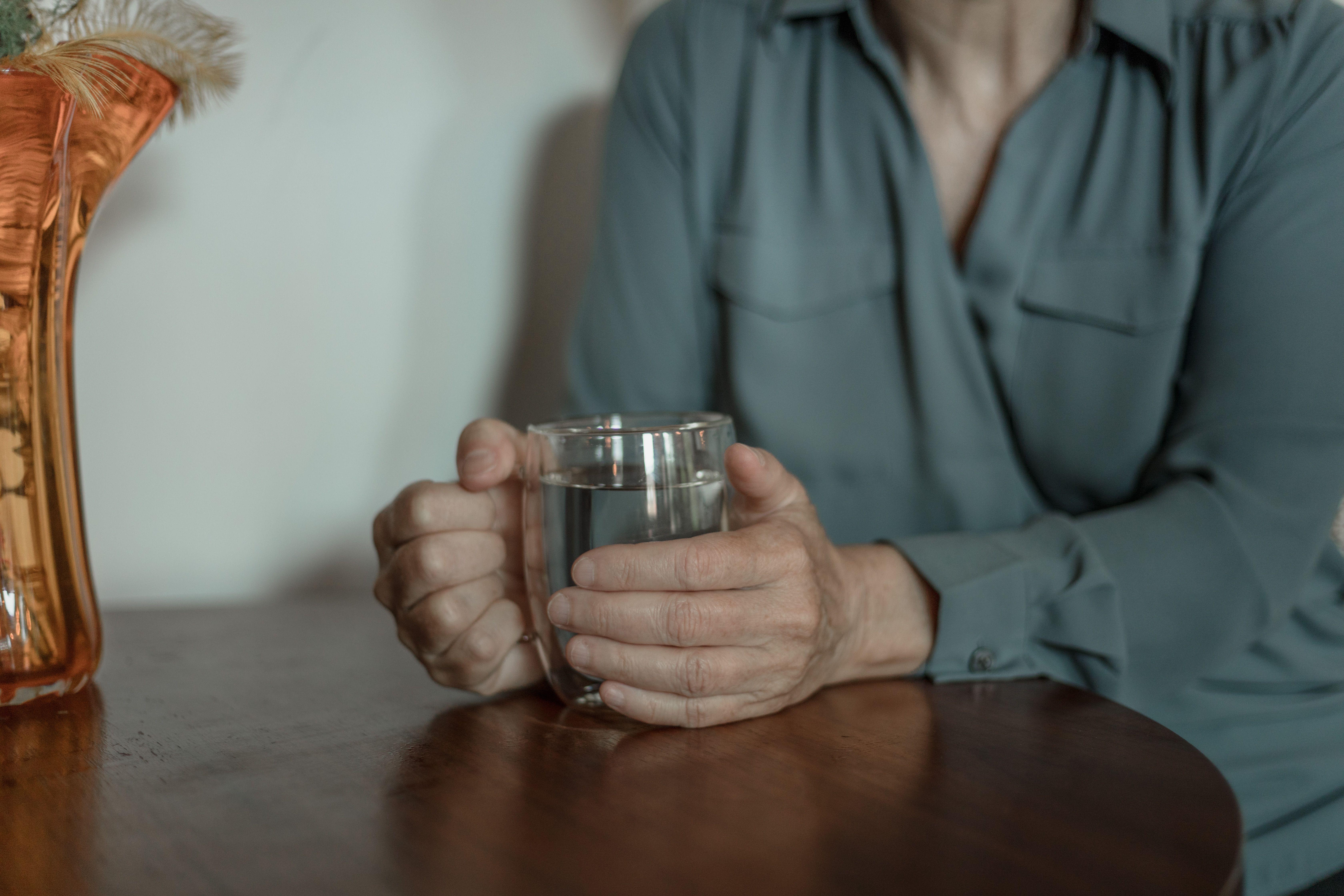 Senior adult's hands holding a glass of water at a wooden table
