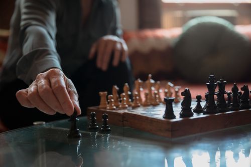 Free An adult in a cozy room makes a thoughtful move on a wooden chessboard. Stock Photo