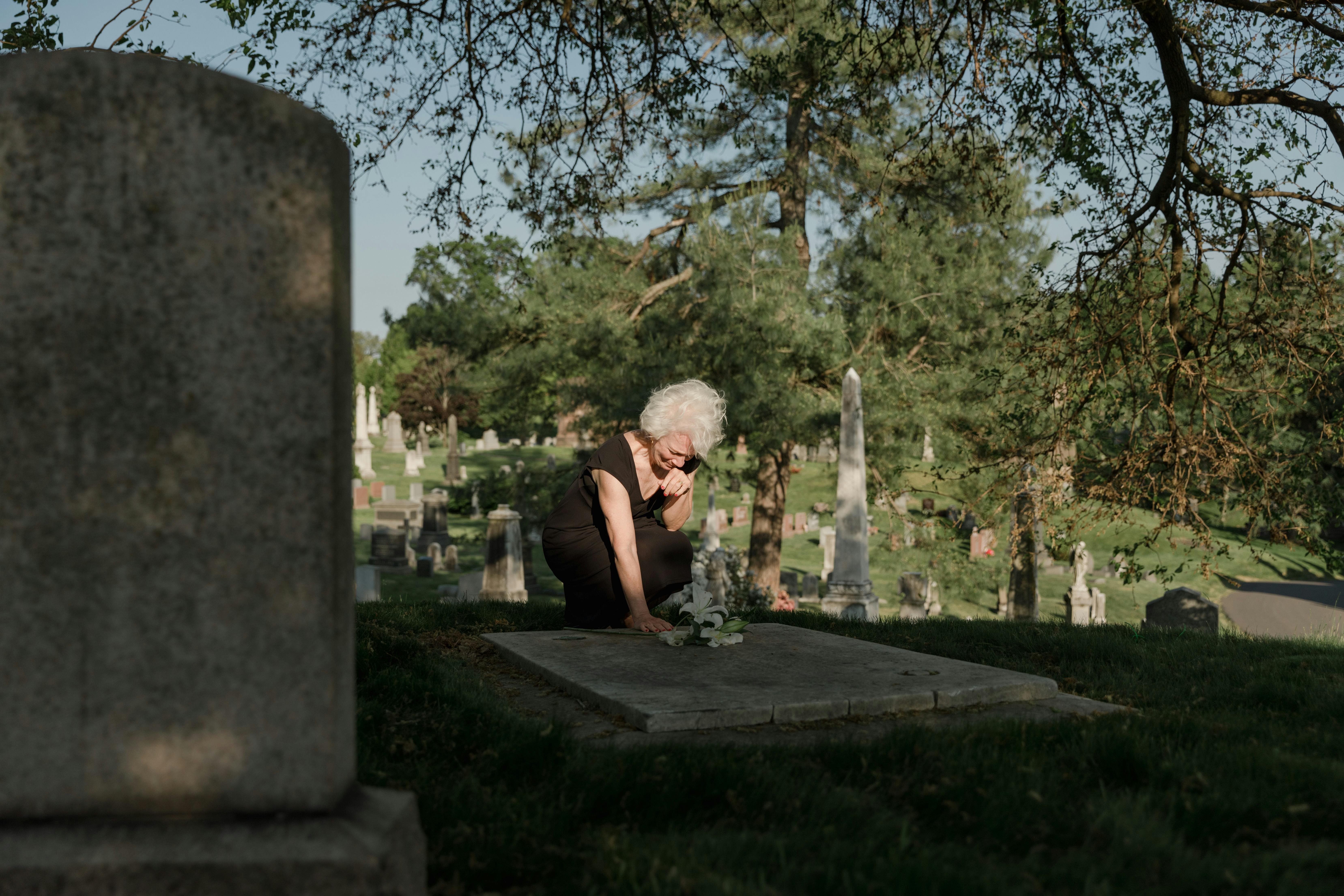 photo of an elderly woman grieving at a grave