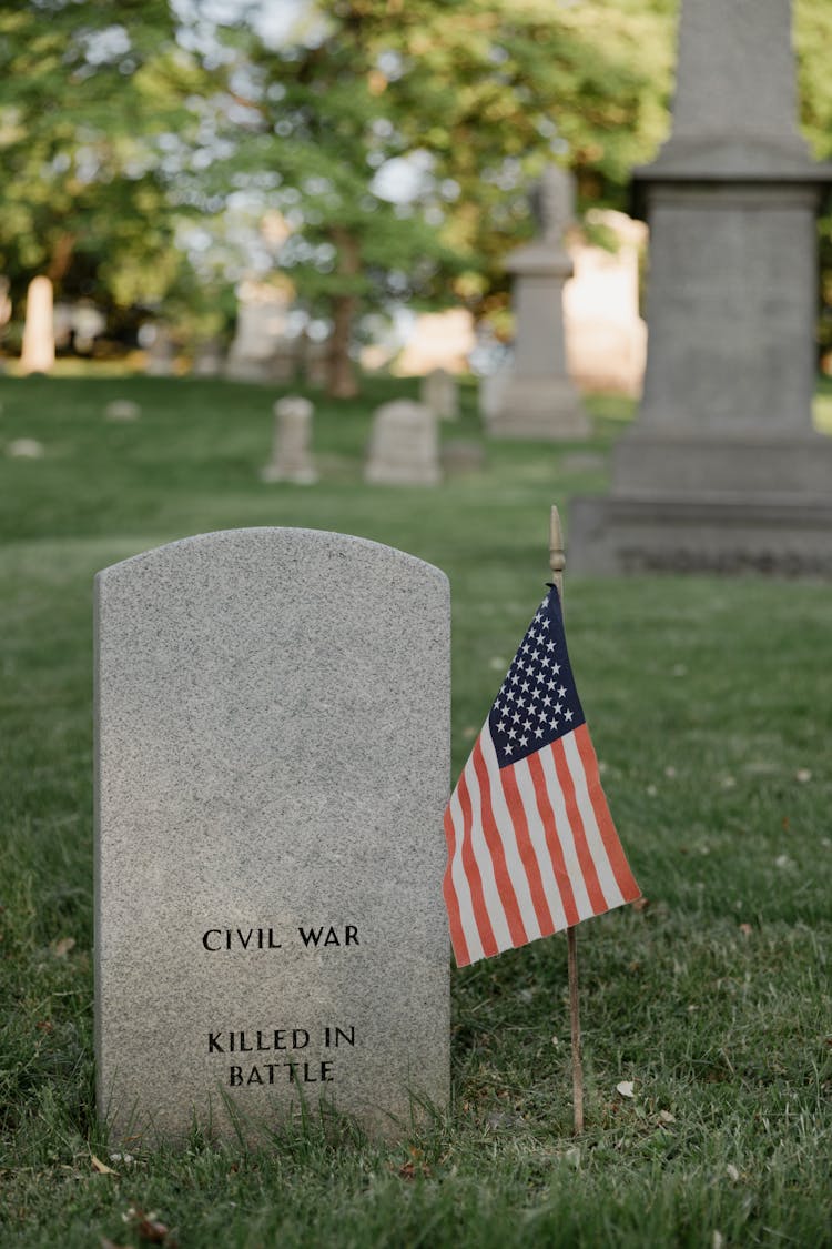 American Flag Beside A Gray Tombstone Of A Veteran