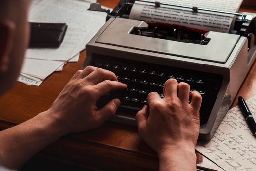 A person typing on a vintage typewriter surrounded by papers in an indoor setting.