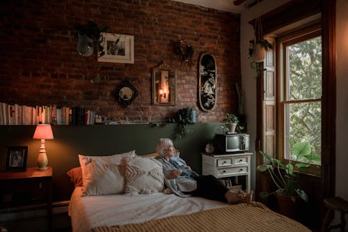 A Elderly Woman Sitting on the Bed while Looking Outside the Window