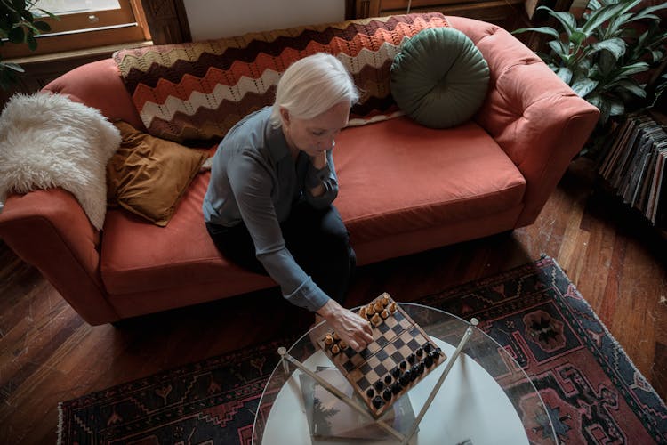 An Elderly Woman Sitting On A Couch Playing Chess Alone