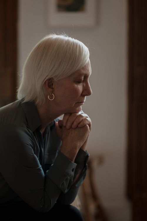 Free Side view of a senior woman with white hair, seated indoors, deeply contemplating. Stock Photo