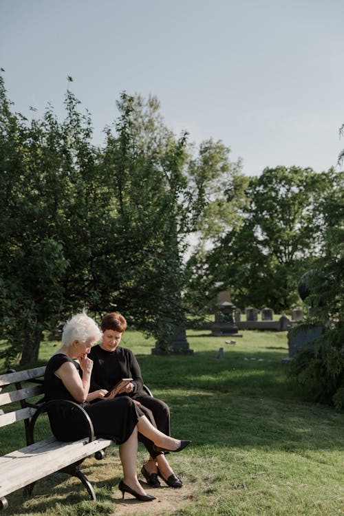 Women Sitting on a Bench Next to a Cemetery 