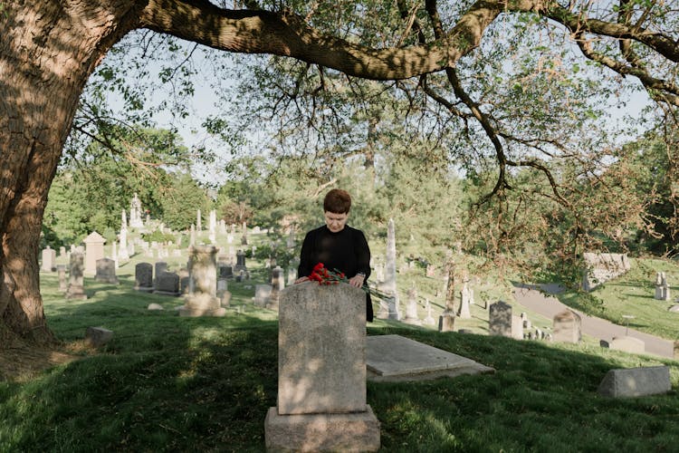 Sad Woman In Black Clothes Bringing Flowers To Grave