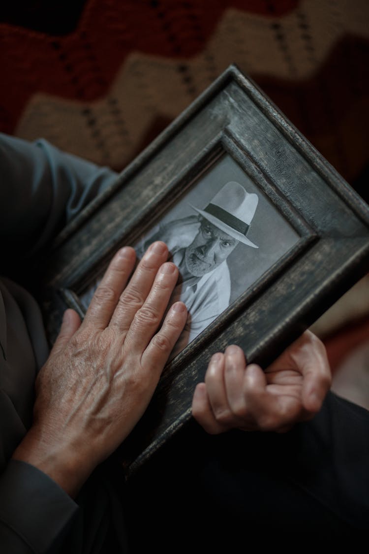 An Elderly Person Holding A Framed Picture Of A Man