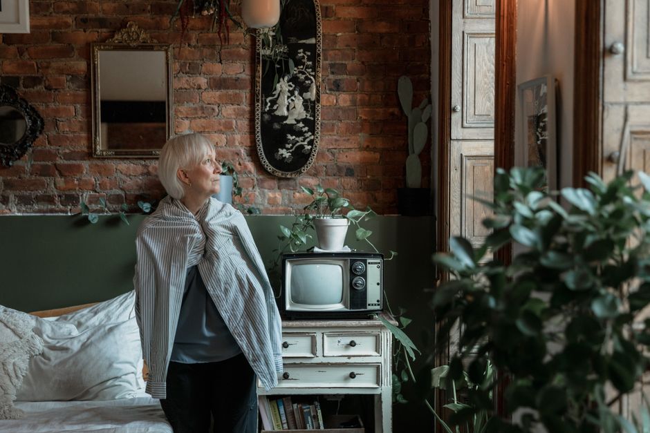 A person looking out of a window in an urban setting, representing the quiet crisis of housing insecurity for older women.
