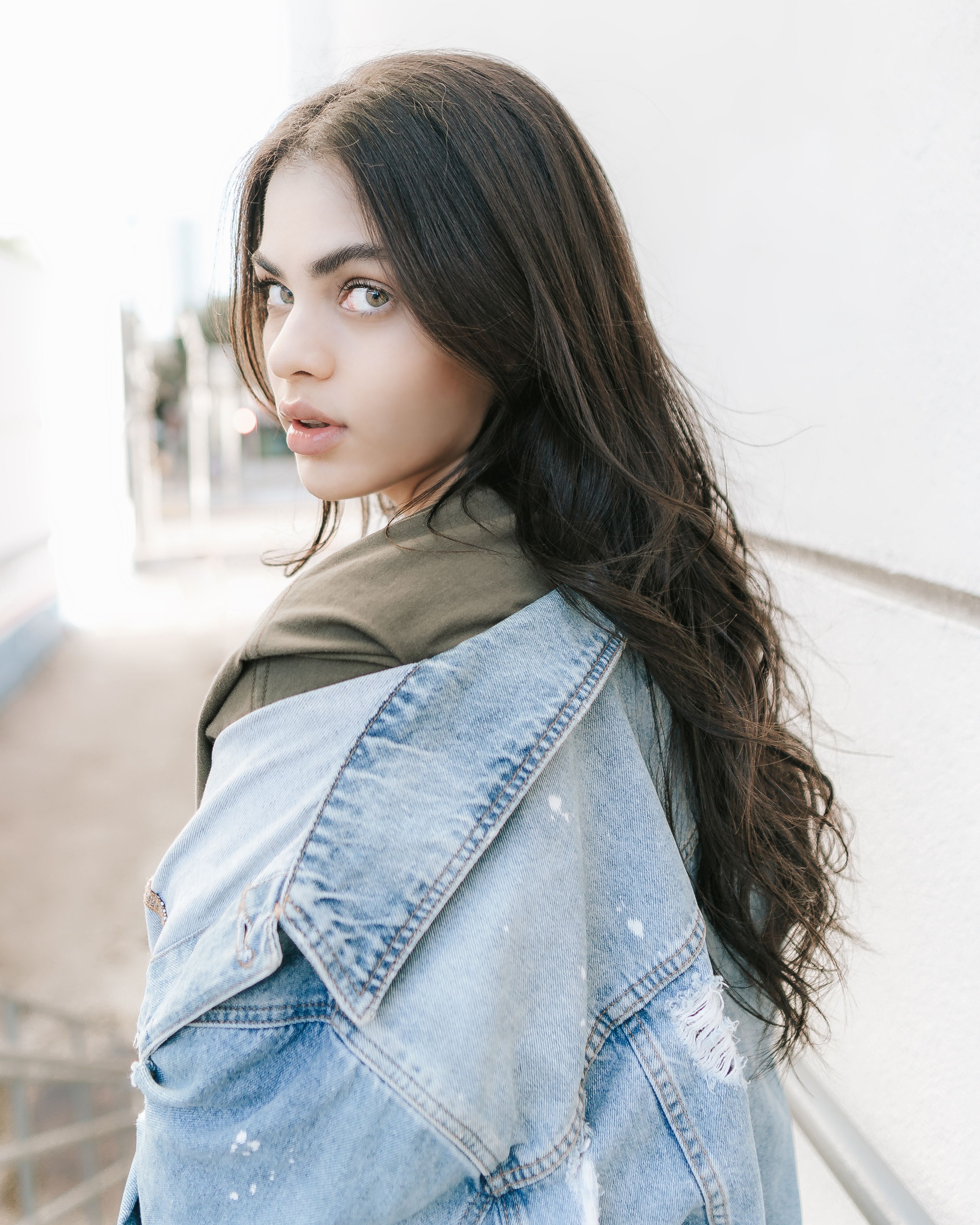A young woman poses with a denim jacket in a bright outdoor day scene.