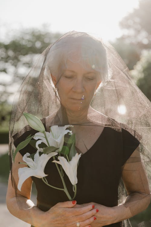 An Elderly Woman Wearing Black Veil while Holding White Flowers