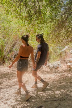 A couple explores a lush forest path, holding hands in the daylight.