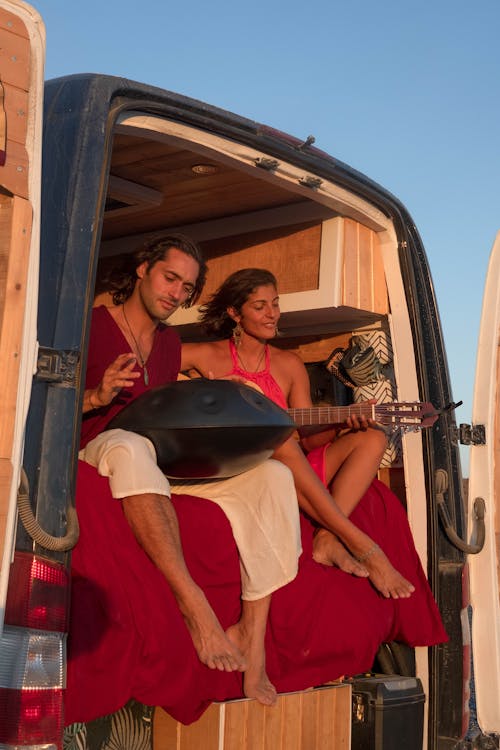 Free Man Playing Handpan Beside a Woman Playing Guitar in a Vehicle Stock Photo