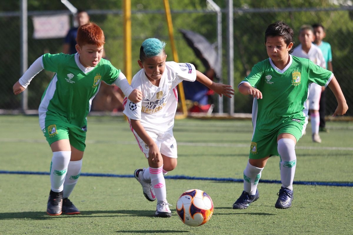 Children playing football together on a green outdoor pitch. Illustrative stock photo.
