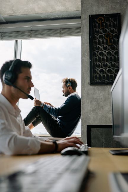 Two men in an office setting wearing headphones and working, showing focused and productive workspace. Two men in an office setting wearing headphones and working, showing focused and productive workspace.