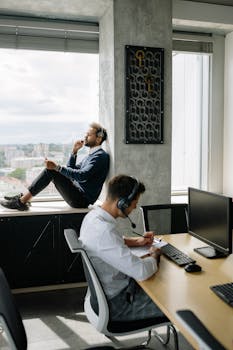 Two men in business attire working in a modern office with computers and headsets, capturing a professional workspace vibe.