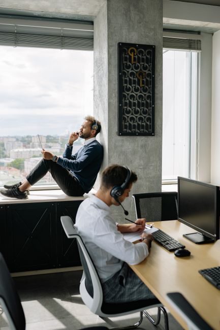Two men in business attire working in a modern office with computers and headsets, capturing a professional workspace vibe.