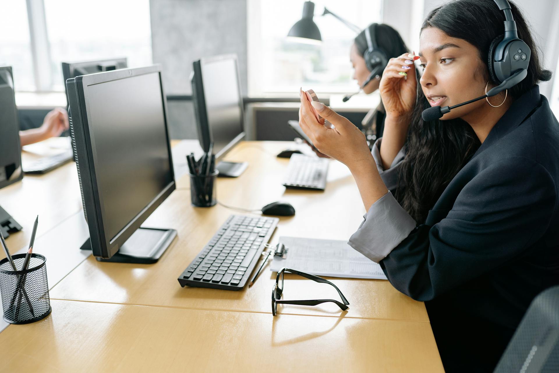 South Asian woman providing customer support in a modern office environment, equipped with a headset.