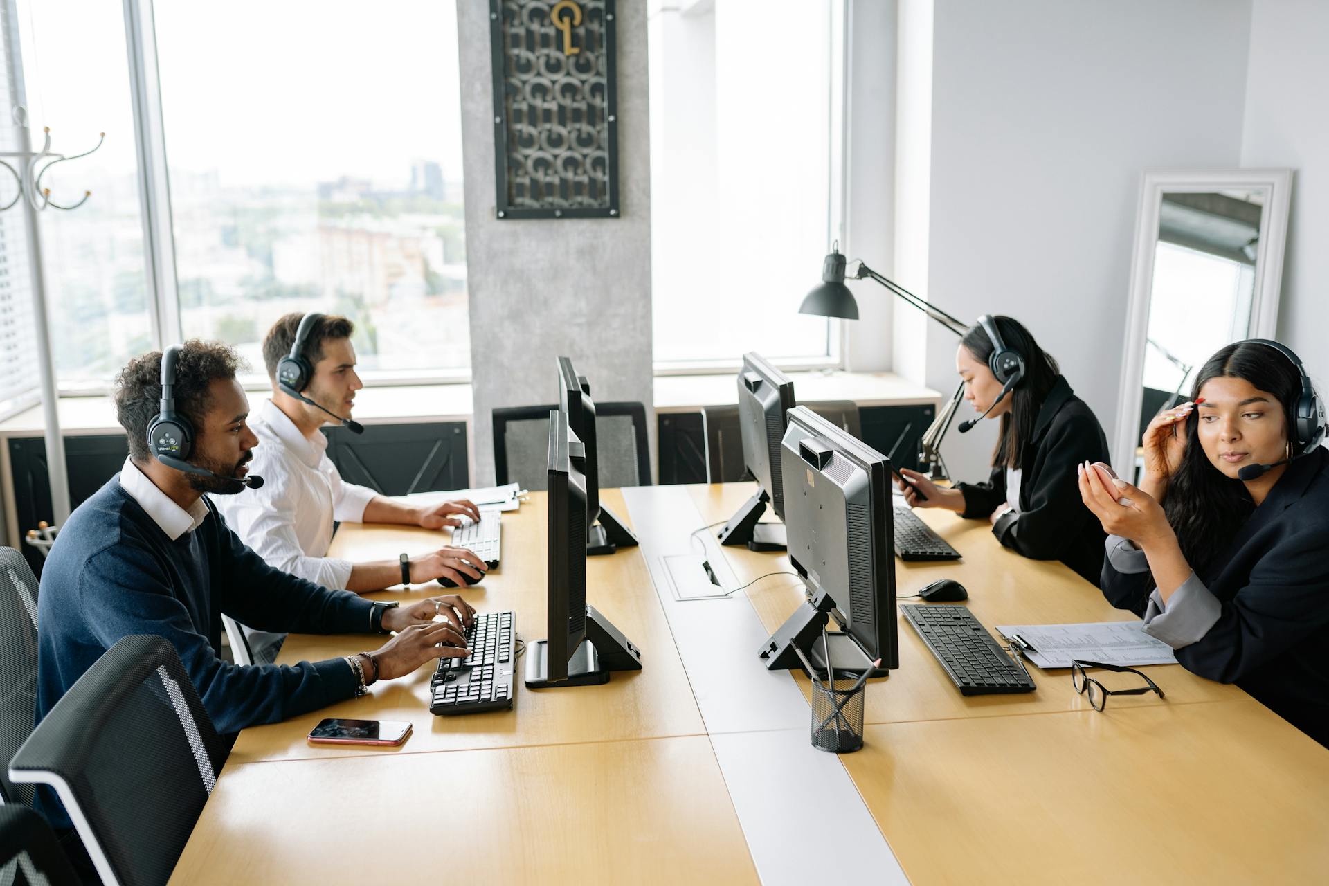 Group of professionals wearing headsets working at computers in an office setting, promoting collaboration.