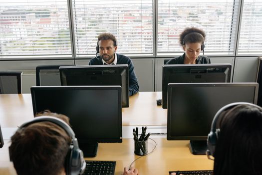 Group of call center agents working on computers in an office environment.