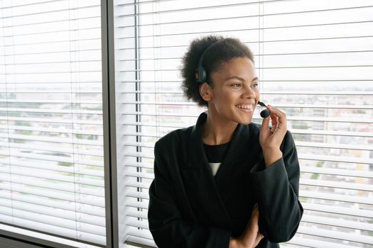 Confident call center employee with headset, smiling at the office window.