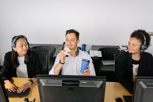 A diverse team of colleagues working at a call center desk with headsets and computers.