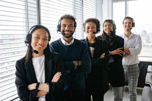 Free A cheerful, diverse team with headsets posing in a bright office environment. Stock Photo