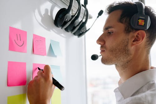 Close Up Photo of Man Writing on Pink Sticky Note