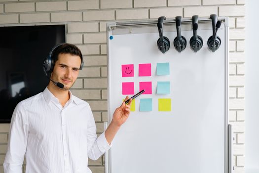 Confident businessman wearing headset, presenting ideas using sticky notes on a whiteboard in modern office.