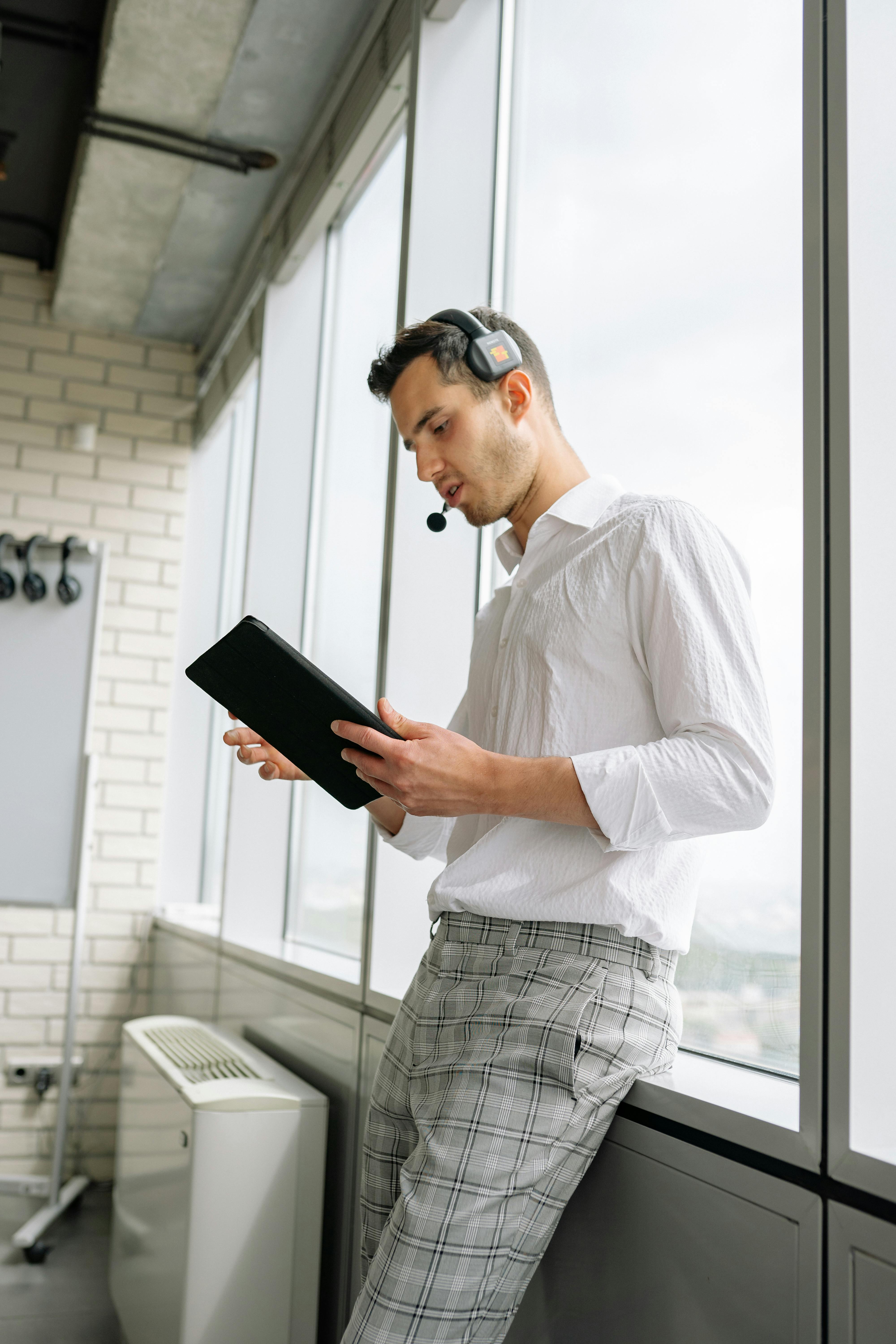 A worker using a tablet and headset beside office windows, representing frontline workflows where agent devices may sit outside the standard PC.