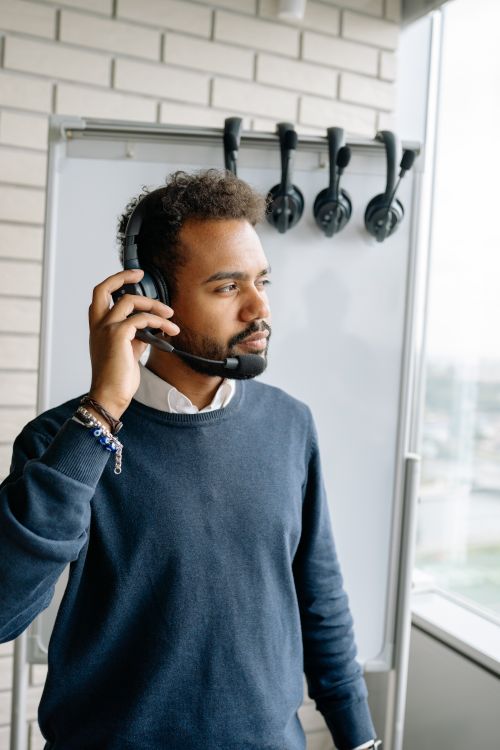 Free African American man wearing headphones and blue sweater by a whiteboard in a modern office. Stock Photo