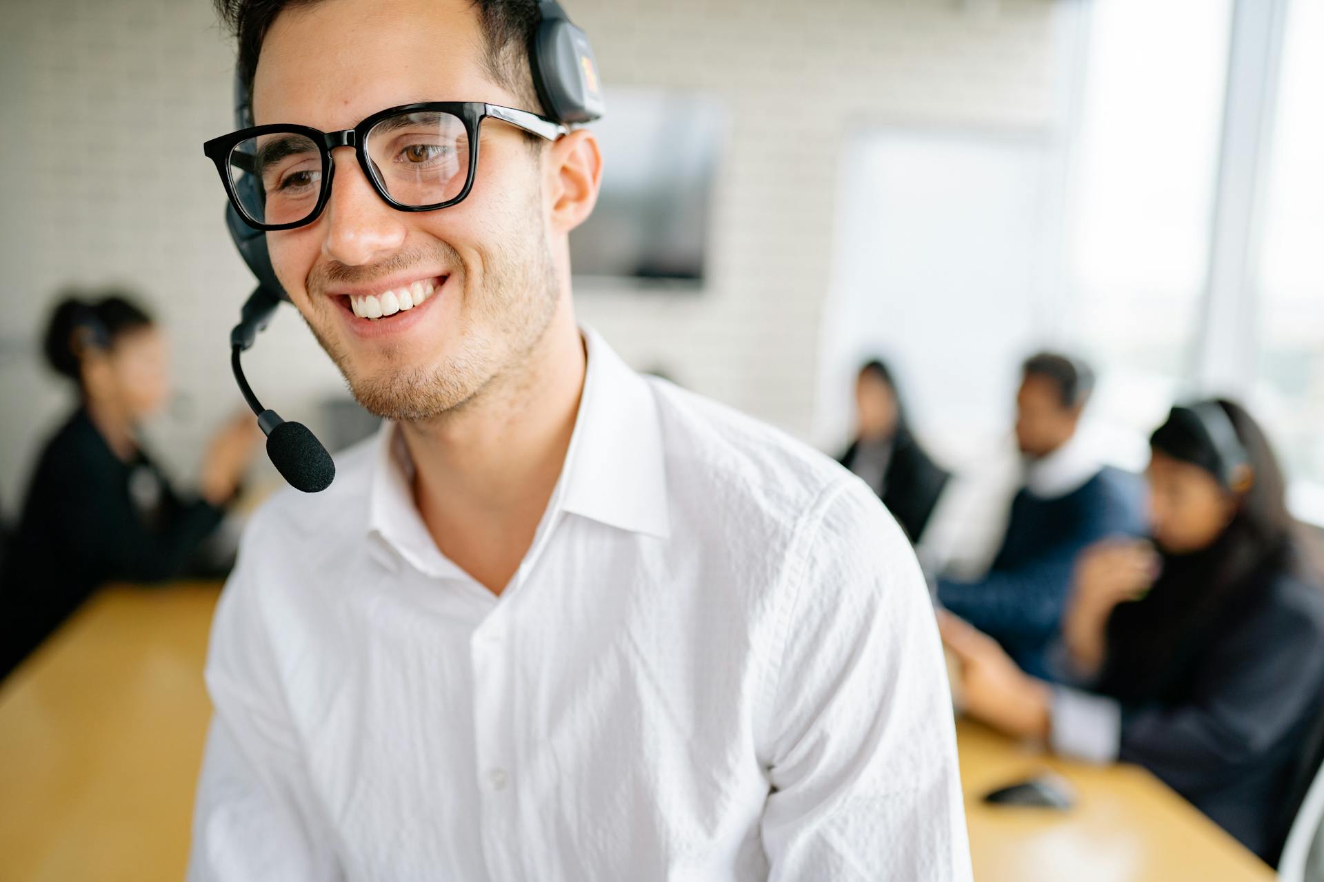 Friendly customer service representative wearing a headset, smiling in a busy office environment.