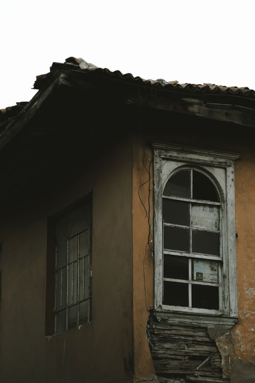Free A rustic, dilapidated house exterior featuring broken windows and weathered walls, captured in a vertical shot. Stock Photo