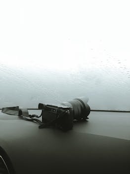 Close-up of a DSLR camera on a car dashboard with raindrops on the windshield, creating a moody effect.
