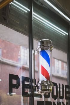 A barber pole with iconic red, white, and blue stripes outside a barbershop.