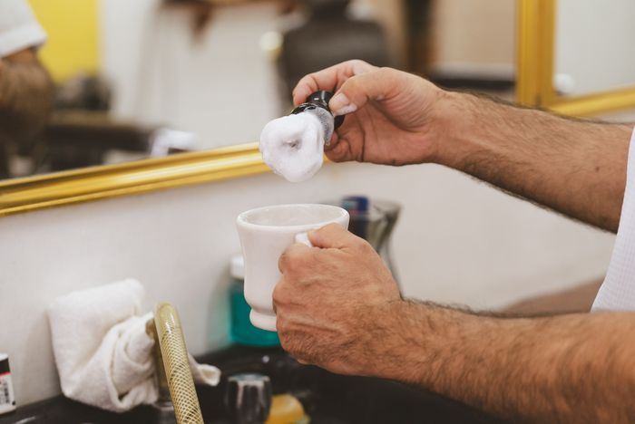 A badger brush loaded with lather over a shaving cup. Photo by Los Muertos Crew on Pexels