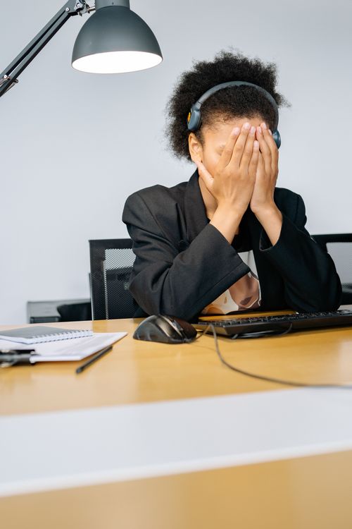 Free A tired call center employee covering her face with hands in frustration, wearing a headset in an office. Stock Photo