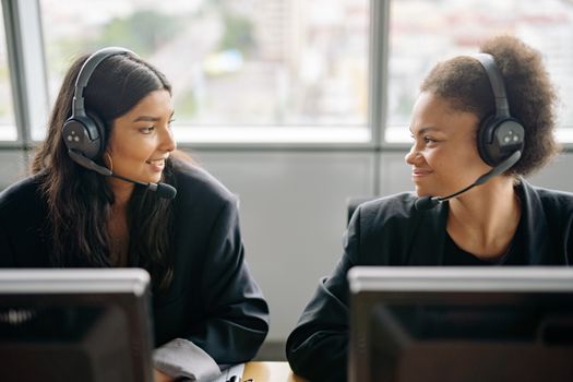 Two smiling female call center agents with headsets engaging in teamwork.