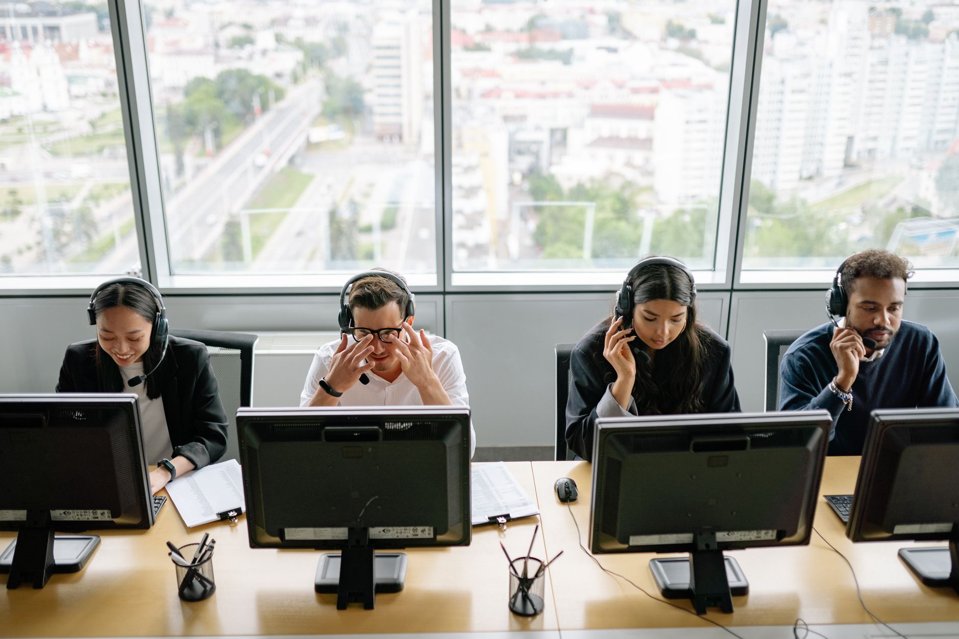 Group of diverse call center employees working at computers in a modern office setting.
