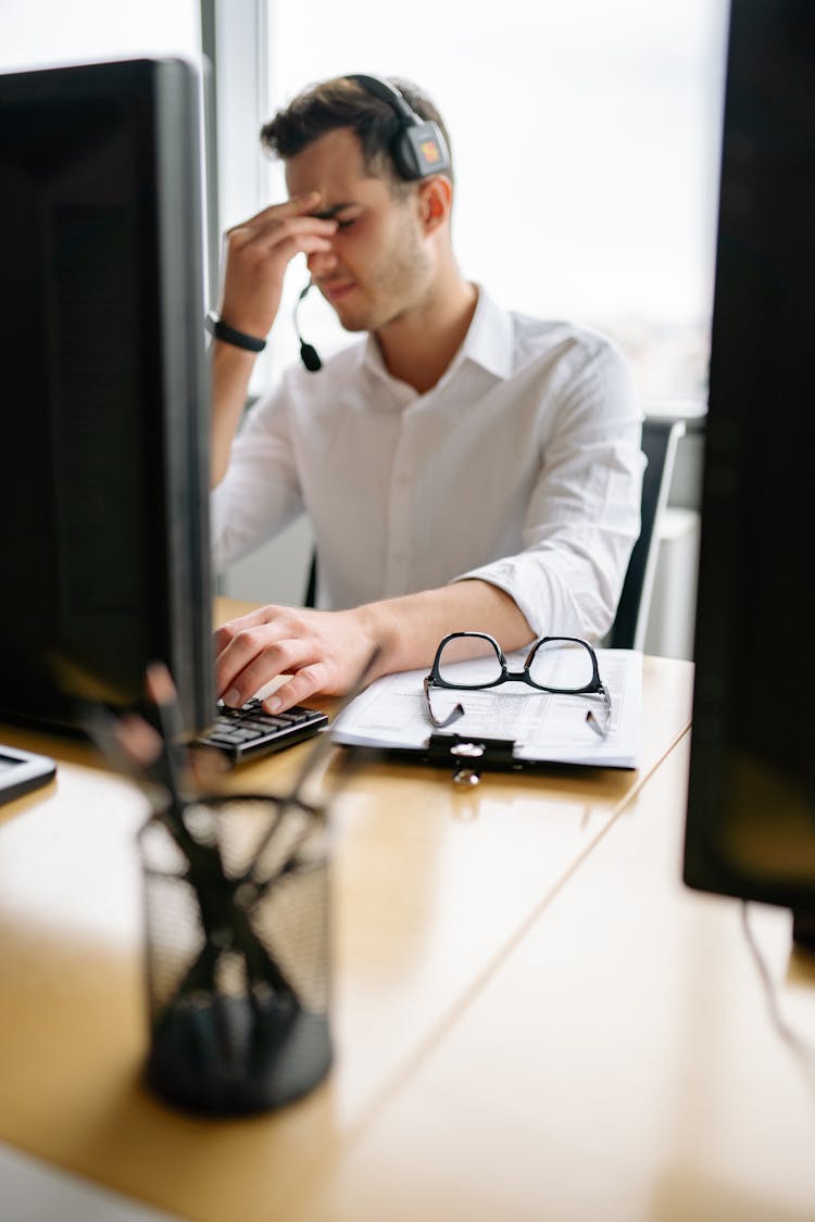 A Tired Man Sitting At His Desk Rubbing His Eyes