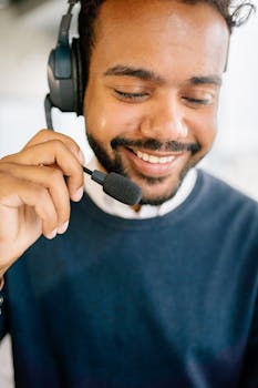 Cheerful call center agent wearing headphones, smiling while holding microphone, in a modern office.