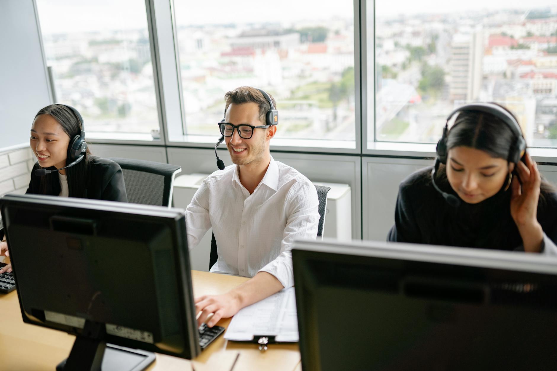 Group of call center employees wearing headsets, collaborating in a bright office environment.