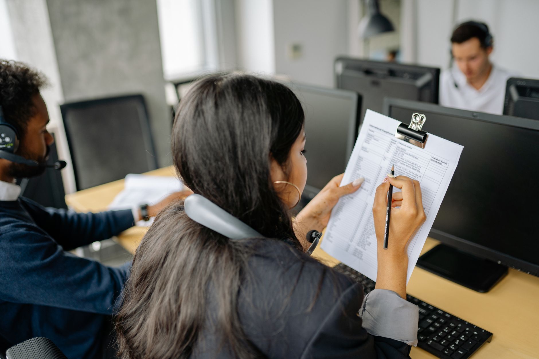 Focused call center employee reviewing documents while on a call in an office setting.