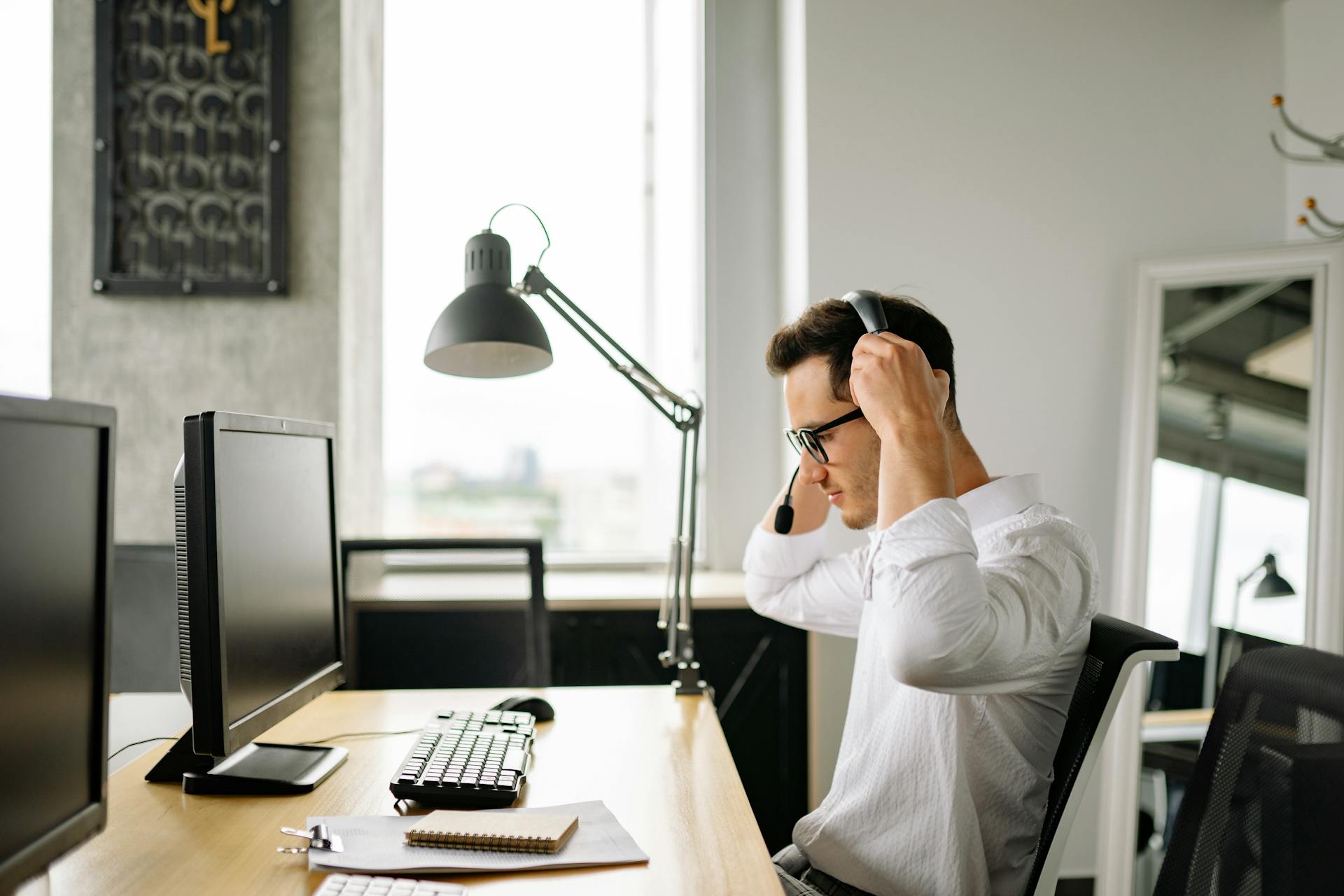 Young man in a call center adjusting headset in a modern office environment.