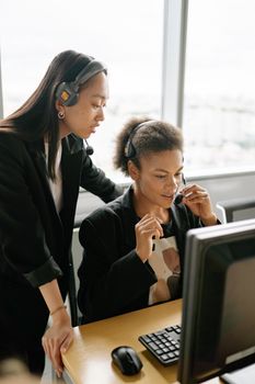 Two diverse women in a call center, collaborating on customer support tasks.